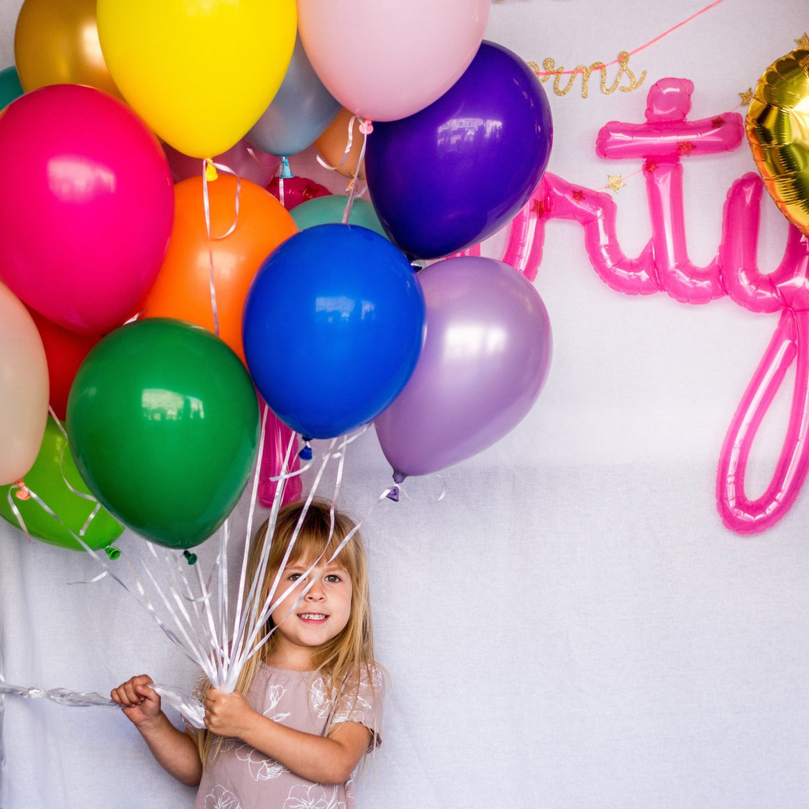 A little girl holding a bouquet of balloons in a variety of colors for her birthday.