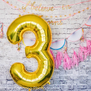 A gold number 3 balloon on a party backdrop.