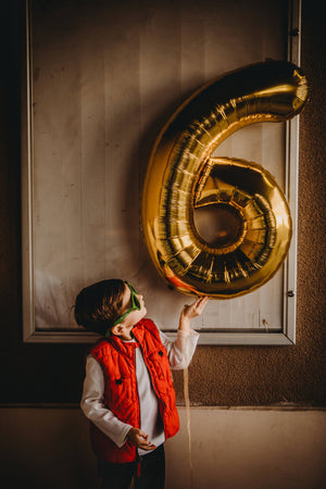 A little boy looking at a huge number 6 balloon.