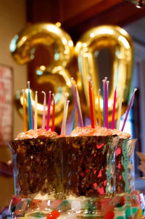 A cake with candles in it and gold 30 balloons in the background.