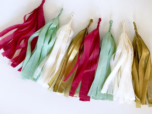 An arial view of a cranberry, sage, cream, and gold tissue tassel garland sitting on a white table.