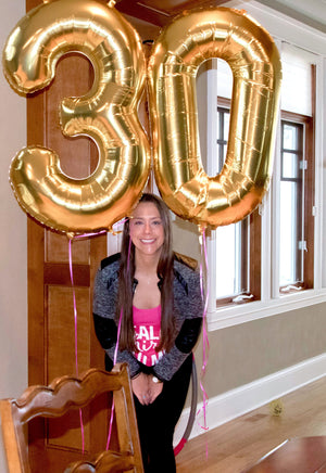A women standing under gold balloons in numbers 30.