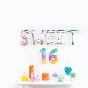 Silver balloon letters that spell SWEET are hanging above two rainbow numbers 16.