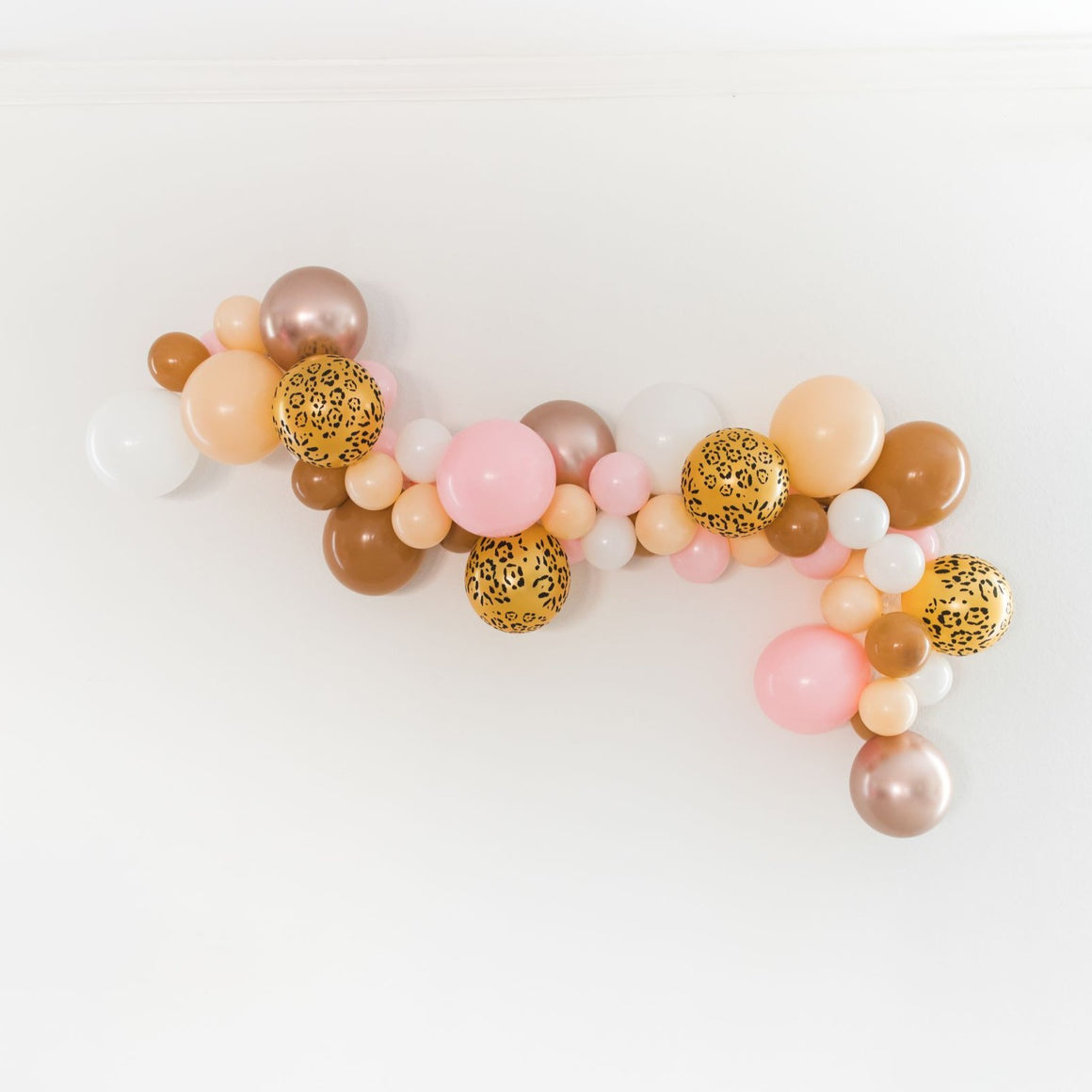 A beautiful bachelorette themed garland is strung across a white wall. The garland is made up of a mix of white, blush, pink, mocha, chrome rose gold, leopard print balloons.