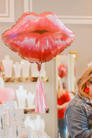 Jumbo red and pink balloon floating next to a woman at a jewelry boutique.