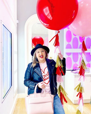 A woman with a big smile is holding a 36 inch bright red balloon with red, pink, and gold tassel tail.