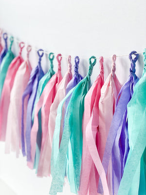 Side angle view of hand rolled tissue tassel garland in the colors pink, blush, lilac, and aqua used in mermaid or princess inspired birthday girl parties, unicorn parties or baby showers.