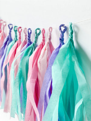 Side view of hand rolled tissue tassel garland in the colors pink, blush, lilac, and aqua used in mermaid or princess inspired birthday girl parties, unicorn parties or baby showers.