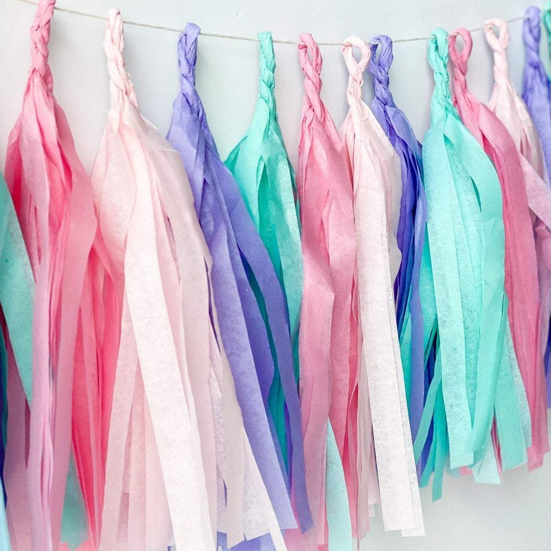 Close up of hand rolled tissue tassel garland in the colors pink, blush, lilac, and aqua  used in mermaid or princess inspired birthday girl parties, unicorn parties or baby showers.