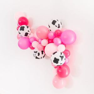 Side view of an 8ft balloon garland on a white wall. Colors are pink, rose, wildberry, neon magenta, and cow print!