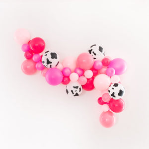 Various pinks and cow print balloons in an 8ft balloon garland on a white wall.