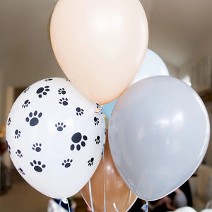 A bundle of four 11 inch balloons in the colors blush, gray, mocha, pastel light blue, and one white balloon with black puppy dog paw prints.