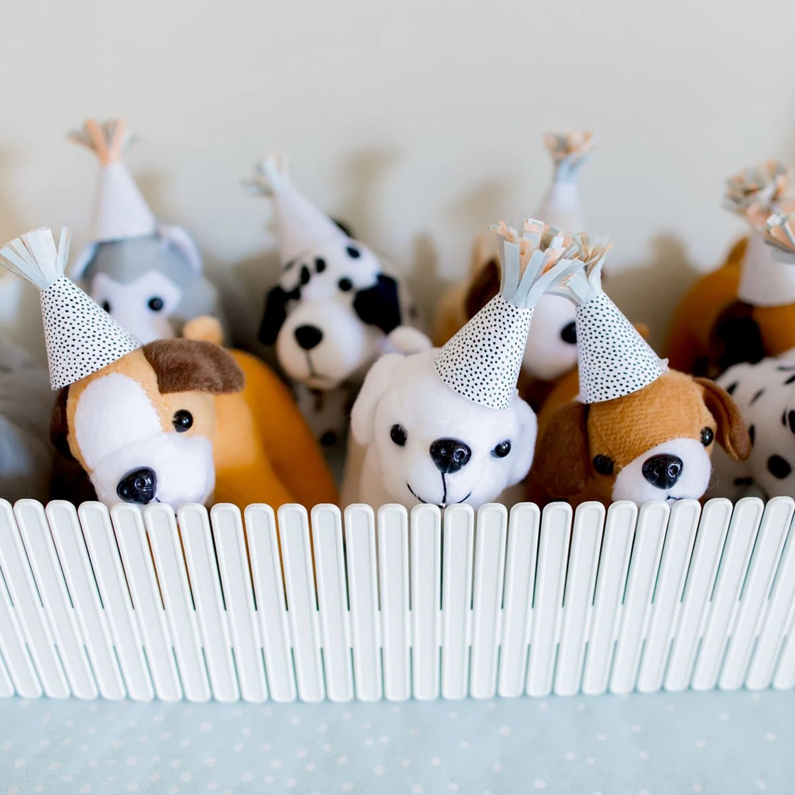 Small stuffed animal dogs wearing party animal hats in a plastic white fence.