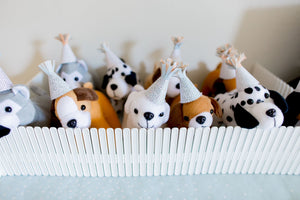 Small stuffed animal dogs wearing party animal hats in a plastic white fence.