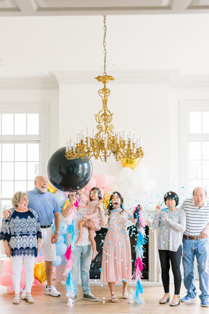 Family popping a 36 inch black latex balloon filled with shades of blue confetti.
