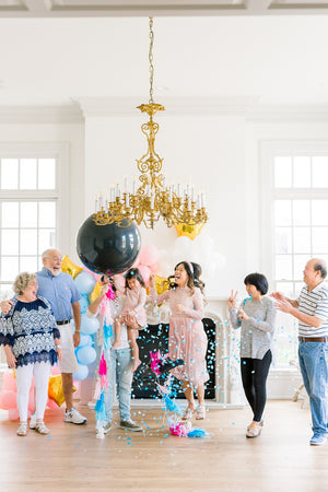 Family celebrating gender reveal after popping a 36 inch black latex balloon filled with shades of blue confetti.