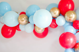 A balloon garland with the colors blue, red, and gold hangs on a white wall 