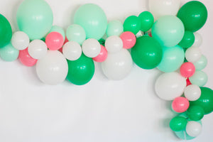 A close up of a balloon garland with the colors white, pastel mint, spring green, rose hanging on a white wall.
