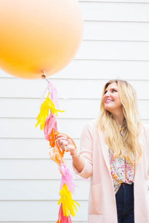 Lady holding a 36 inch balloon in the color blush with pink and yellow tassels on string.