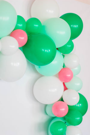 Side view of aballoon garland with the colors white, pastel mint, spring green, rose hanging on a white wall.