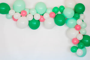 A balloon garland with the colors white, pastel mint, spring green, rose hangs on a white wall.