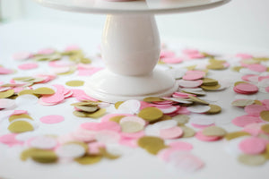 Top view of 1 inch handcut confetti circles in the colors pink, blush, white, and gold sitting on a white table. There is a white frosting cupcake sitting on a white cake stand.