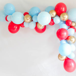 A balloon garland with the colors blue, red, and gold hangs on a white wall 