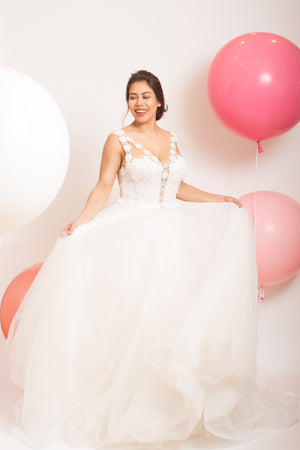 A girl holding her white dress and three jumbo balloons.