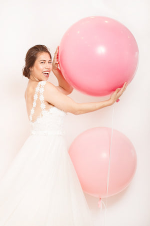 A girl is holding a rose colored balloon.