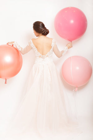 Woman in a long white dress is holding three jumbo balloons in different shades of pink. 